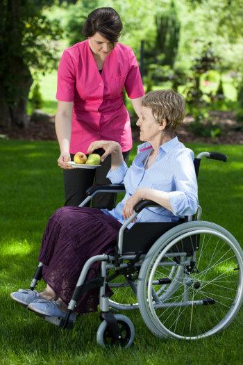 Caregiver walking with a senior in a wheelchair through a garden